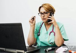 Eine Medizinerin sitzt mit Telefon und Stethoskop vor einem Computer. Foto: Karolina Grabowska/Pexels