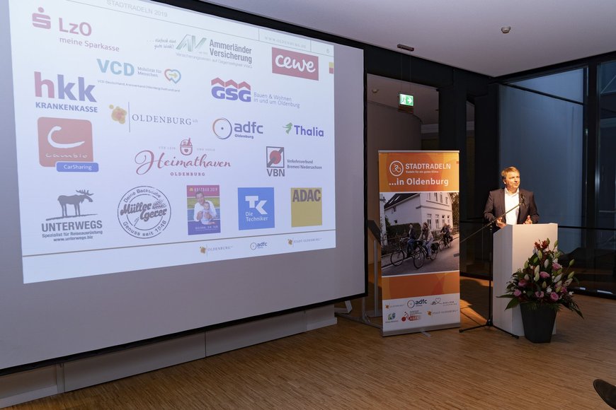 Oberbürgermeister Jürgen Krogmann bedankt sich bei den Unterstützern von STADTRADELN, deren Logos auf einer Leinwand zu sehen sind. Foto: Stephan Walzl