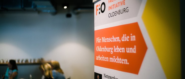 Roll-up der Fachkräfte-Initiative Oldenburg (FIO), im Hintergrund Gruppenarbeitsphase während eines Fachkräfte-Forums. Foto: Jörn Tempel