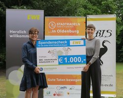 Marion Rövekamp, Vorständin der EWE AG, übergibt den Scheck für das Erreichen des dritten Etappenziels an Tara Fyson von IBIS e.V. Foto: Stadt Oldenburg