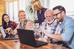 Junge Personen helfen Älteren mit Computern. Foto: Mediteraneo/AdobeStock