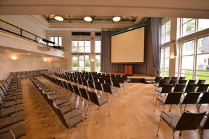 Veranstaltungssaal PFL, Blick von der hinteren rechten Ecke auf die Bühne mit heruntergelassener Leinwand. Foto: Jörg Hemmen.