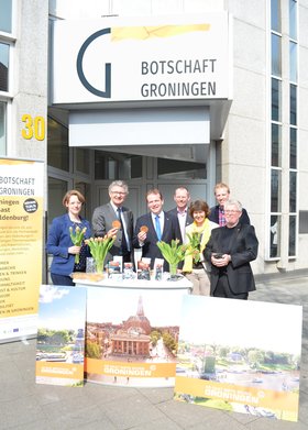 Pressekonferenz zur Botschaft Groningen: Im Hintergrund ist das Logo zu sehen, auf einem Tresen stehen Tulpen, die Beteiligten halten Sirupwaffeln in der Hand. Foto: Stadt Oldenburg