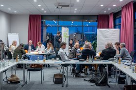 Beim interkommunalen Austausch Ende November 2024 auf Einladung der Stadt Oldenburg anlässlich des integrierten Stadtentwicklungskonzepts (ISEK) gab es viele gute Impulse und Schnittmengen. Foto: plan zwei Menschen sitzen an drei Tischen zusammen und sprechen miteinander. Foto: plan zwei