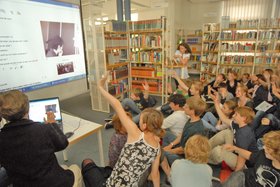 Jugendliche sitzen gemeinsam vor einer großen Leinwand, auf der ein Bild des Videoanrufs zu sehen ist. Foto: Philipp Herrnberger