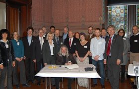 Die Mitglieder der Delegation aus Kinston upon Thames gemeinsam mit Oberbürgermeister Gerd Schwandner und anderen Oldenburgern, stehen um den Tisch mit dem Gästebuch, in das sich eine Person einträgt. Foto: Stadt Oldenburg