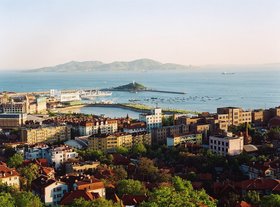 Luftbild, im Vordergrund sind Gebäude zu erkennen, im Hintergrund das Meer und eine bergige Insel. Foto: Stadt Qingdao