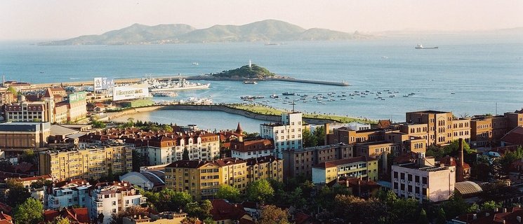 Luftbild, im Vordergrund sind Gebäude zu erkennen, im Hintergrund das Meer und eine bergige Insel. Foto: Stadt Qingdao