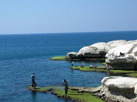 Küste im Landkreis Mateh Asher. Foto: Matte Asher Regional Council Blaues Meer, blauer Himmel und weiße Felsen. Am Ufer stehen zwei Menschen und angeln. Foto: Matte Asher Regional Council