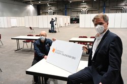 Der Leiter der Feuerwehr, Michael Bremer (links), und Oberbürgermeister Jürgen Krogmann mit einem Schild mit dem Logo des Impfzentrums. Foto: Sascha Stüber Der Leiter der Feuerwehr, Michael Bremer (links), und Oberbürgermeister Jürgen Krogmann mit einem Schild mit dem Logo des Impfzentrums. Foto: Sascha Stüber