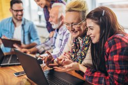 Junge Personen helfen Älteren mit Computern. Foto: Mediteraneo/AdobeStock