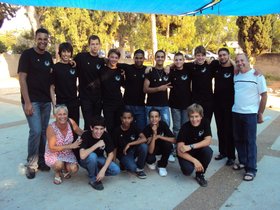 Gruppenfoto, in der vorderen Reihe sitzen einige Personen auf dem Boden, alle tragen schwarze T-Shirts mit dem gleichen Logo. Foto: Edna Taff