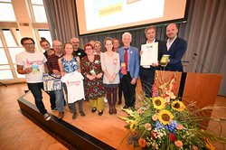 Eine Gruppe Menschen steht mit Jürgen Krogmann auf einer Bühne. Krogmann hält die Auszeichnungsurkunde in den Händen. Foto: Torsten von Reeken