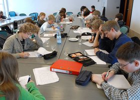 Vertieft in die Arbeit: Teilnehmerinnen und Teilnehmer der Schreibwerkstatt sitzen an einem langen Tisch und schreiben. Foto: Peter Kreier