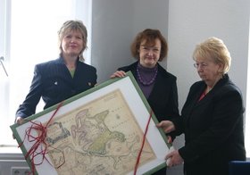 Landrätin von Rügen Kerstin Kassner und Kreistagspräsidentin Gisela Lemke und Rita Schilling halten ein großes gerahmtes Bild mit einer Schleife. Foto: Stadt Oldenburg