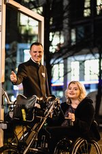 Einer Frau mit Handybike wird die Tür aufgehalten. Foto: gesellschaftsbilder.de/Weiland