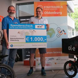 Michael Ottens, Geschäftsführer von ol-e urban:Mobil (rechts im Bild), übergibt den Scheck für das Erreichen des zweiten Etappenziels an Stephan Mickoleit von der Bahnhofsmission Oldenburg. Foto Stadt Oldenburg