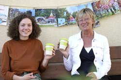 Die Mitarbeiterinnen von StoP sitzen auf einer Bank und halten zwei Kaffeebecher mit dem Logo des Projekts in den Händen. Foto: Stadt Oldenburg