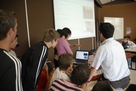 Schülerinnen und Schüler sitzen am Laptop, im Hintergrund eine Leinwand mit dem Livebild eines Videoanrufs. Foto: Philipp Herrnberger