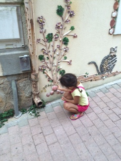 Ein kleines Mädchen hockt vor einer Hauswand und sieht sich eine Verzierung in Form einer Blumenranke an an. Foto: Theresa Bartels